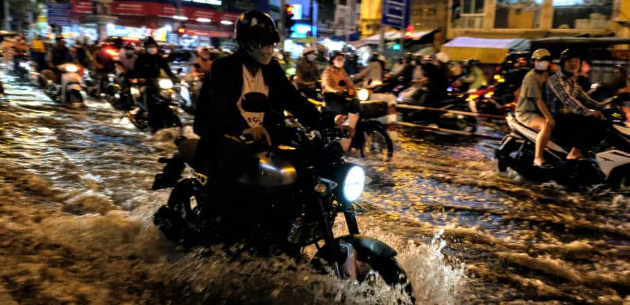 Motorbikes are driving through heavily flooded streets.