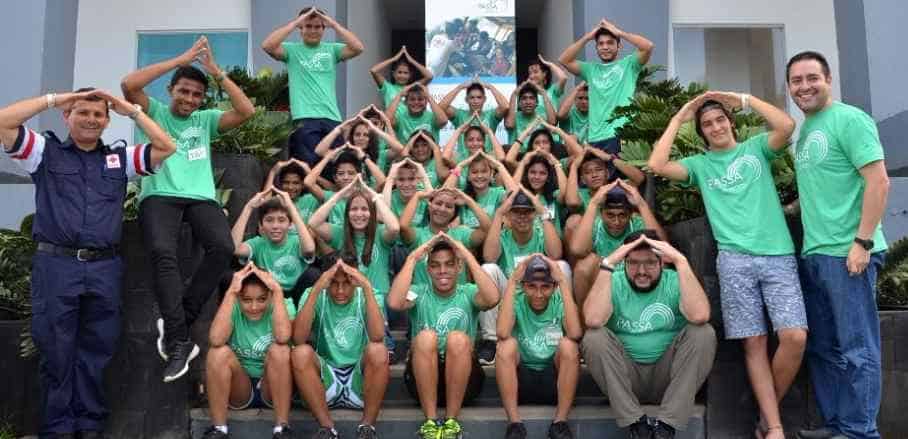 A group picture of people wearing green PASSA shirts holding their hands like a roof over their heads.